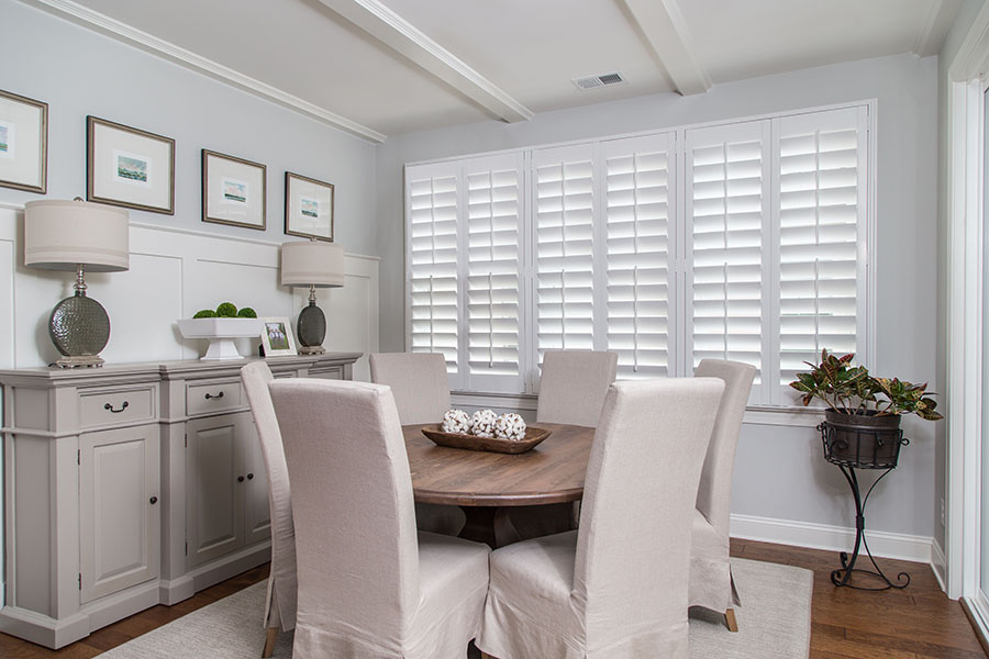 White Polywood shutters are a great option to insulate your picture windows. White Polywood shutters on a large picture window within a medium-sized dining room.