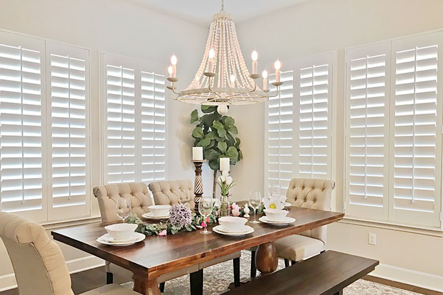 Resistant to moisture and temperature extremes, versatile Polywood shutters are suitable for any environment, including this stylish dining area. White Polywood shutters in a corner of a beige dining room.