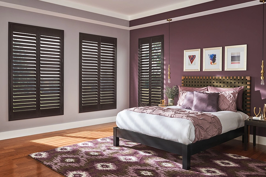 Premium wood shutters are built to last longer than many other window treatments. Dark wood ovation shutters within three windows inside a bedroom