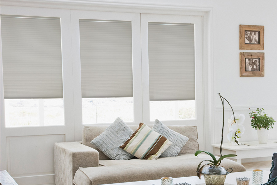 Cellular shades are energy-efficient for your living spaces.  Light gray cellular shades on three separate windows in large light wood and beige colored living room.