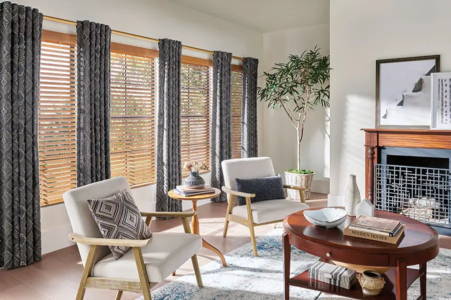 Installing new window treatments is an easy way to update a room's decor instantly. Wood blinds and gray patterned drapes on windows in a contemporary living room